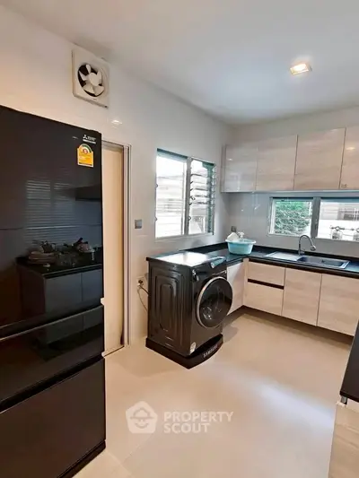 Modern kitchen with sleek appliances and ample natural light, featuring a washing machine and spacious layout.