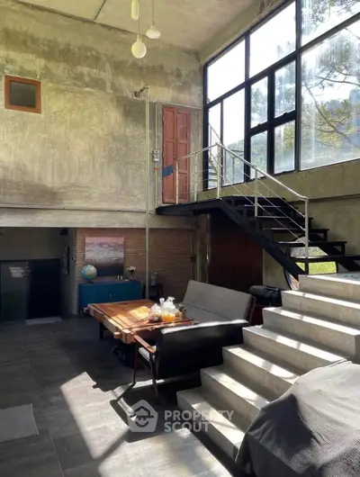 Spacious industrial-style living room with large windows and modern staircase