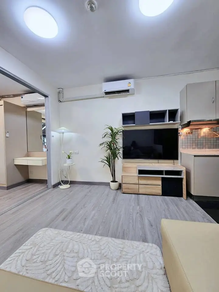 Modern living room with sleek furniture and open kitchen layout, featuring stylish flooring and bright lighting.