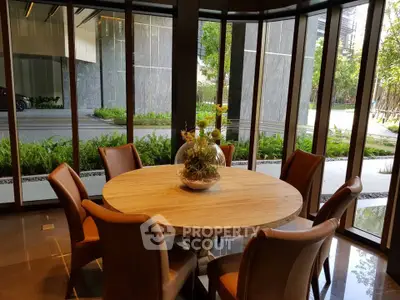 Elegant dining area with round wooden table and leather chairs, surrounded by floor-to-ceiling windows offering lush garden views.