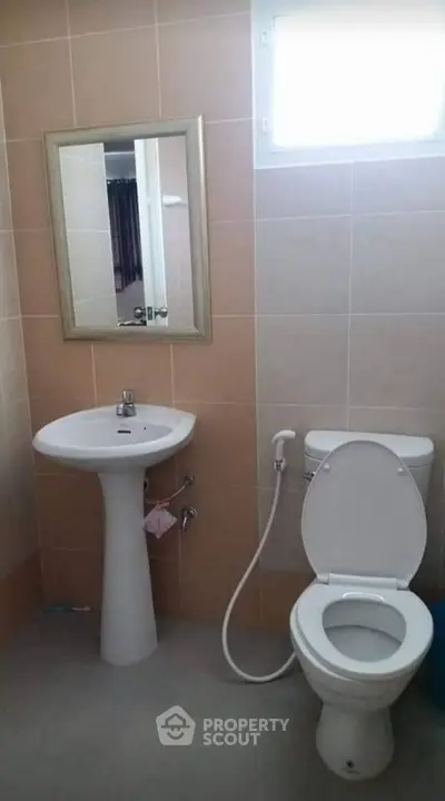 Modern bathroom with pedestal sink and toilet, featuring neutral tiles and natural light.