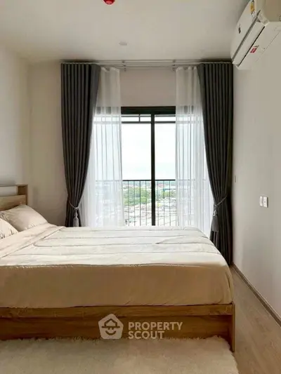 Modern bedroom with large window and city view, featuring elegant curtains and cozy bedding.