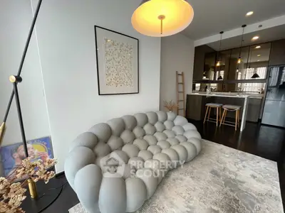 Modern living room with unique sofa and open kitchen layout, featuring stylish decor and contemporary lighting.