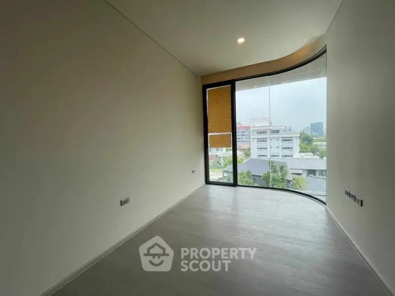 Spacious room with large window offering city view in modern apartment