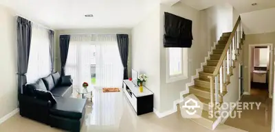 Modern living room with staircase and natural light, featuring sleek black sofa and elegant decor.