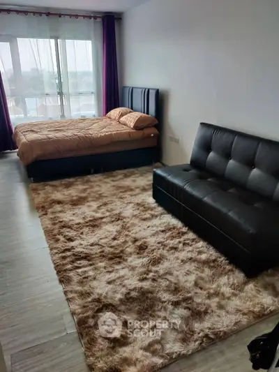 Modern studio apartment with cozy bed and stylish sofa, featuring large windows and plush carpet.