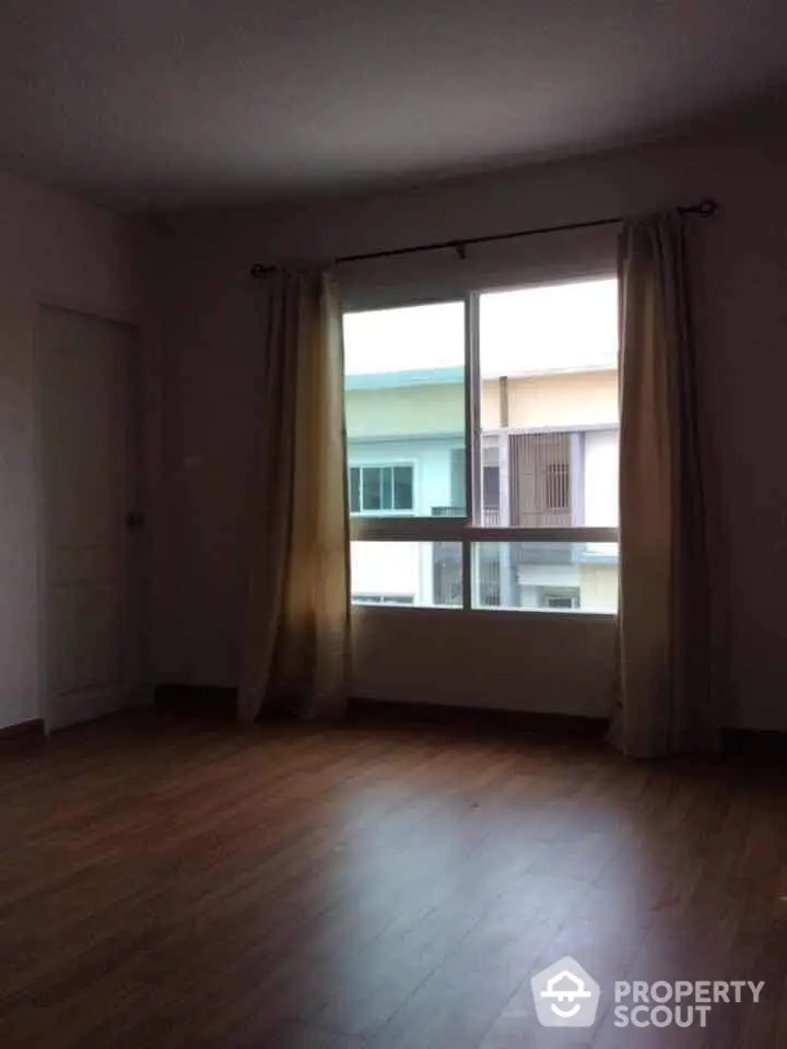 Spacious and well-lit empty room with hardwood floors and large window, ready for personalization in a residential building.