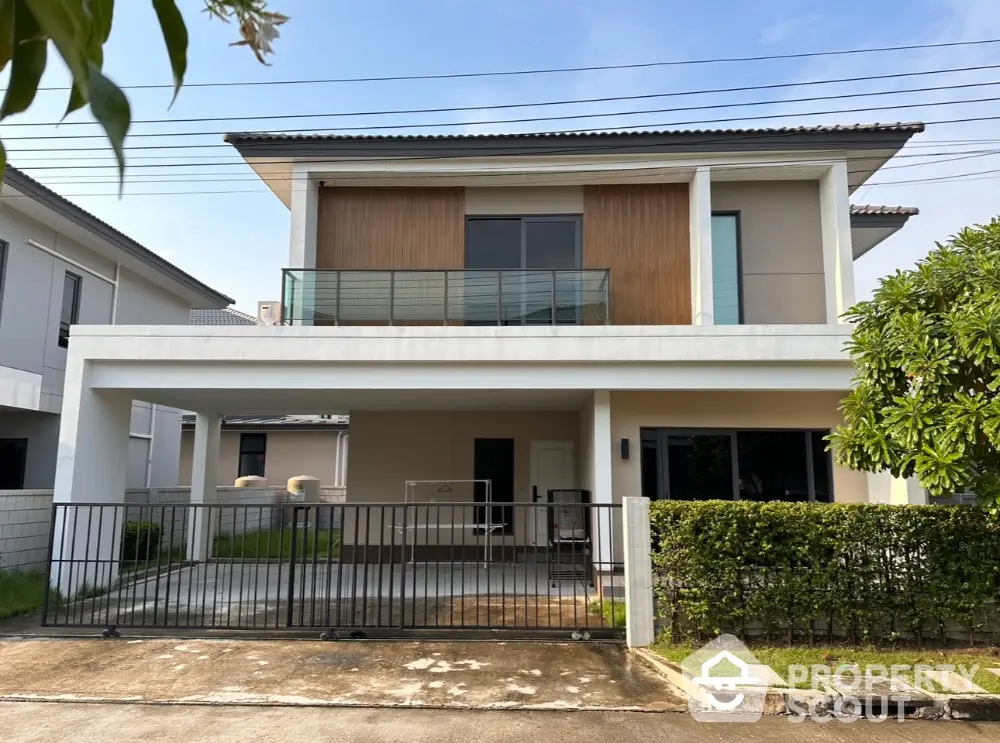 Modern two-story house with spacious balcony and lush greenery in a serene neighborhood.