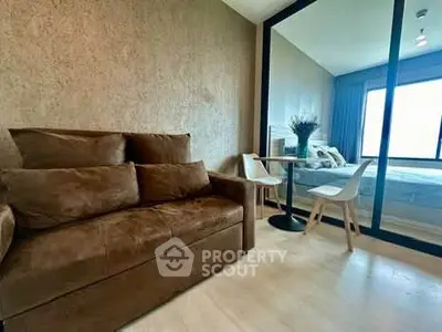 Modern living room with brown sofa and glass partition to bedroom, featuring stylish decor.