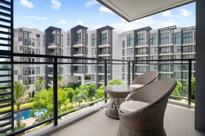 Modern apartment balcony with wicker chairs overlooking lush garden and pool in luxury complex.
