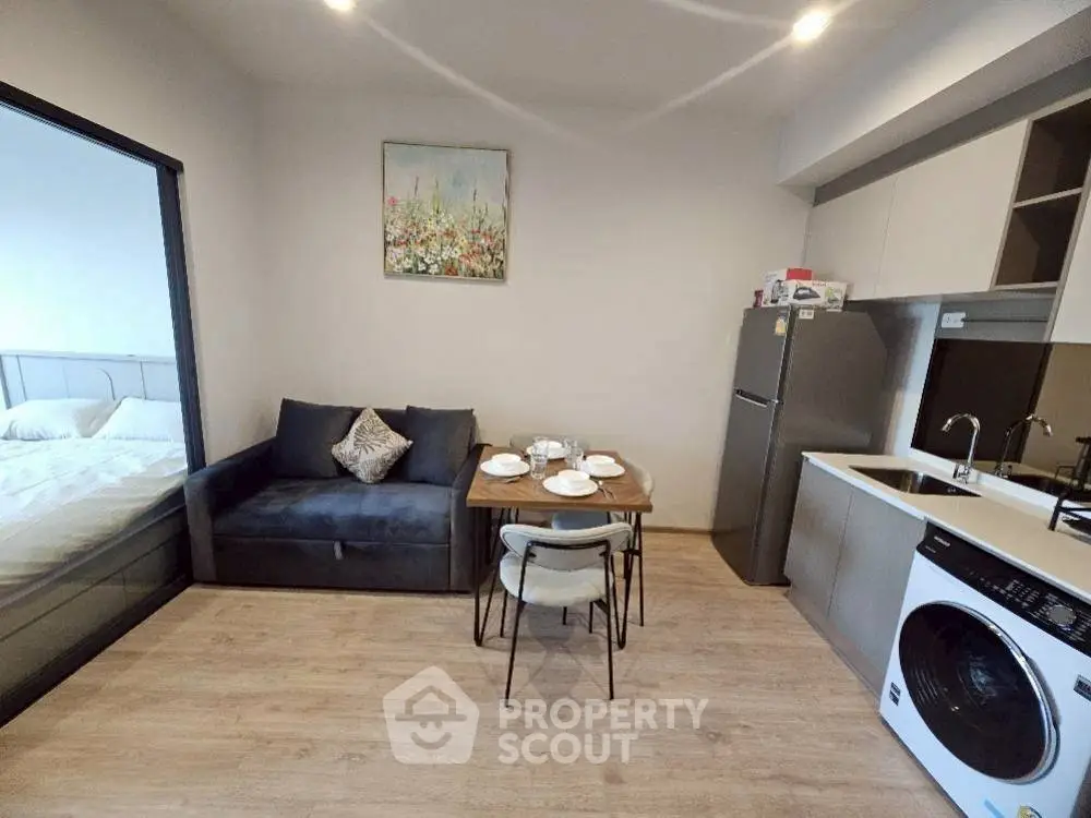Modern apartment interior with cozy living area and kitchen featuring washing machine and fridge.