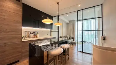 Modern open-layout kitchen with sleek black cabinetry and cozy living area, featuring stylish pendant lighting.