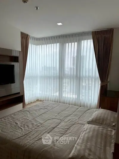 Spacious bedroom with large windows and modern decor in a high-rise apartment.