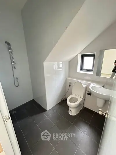 Modern bathroom with sleek design and efficient use of space, featuring a shower and toilet under sloped ceiling.