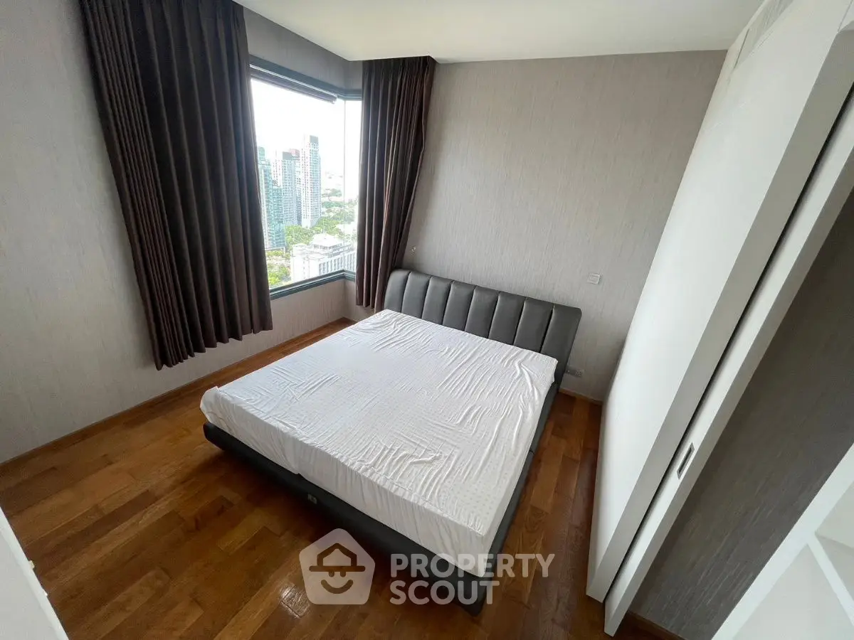 Spacious bedroom with large window offering stunning city views in modern apartment.