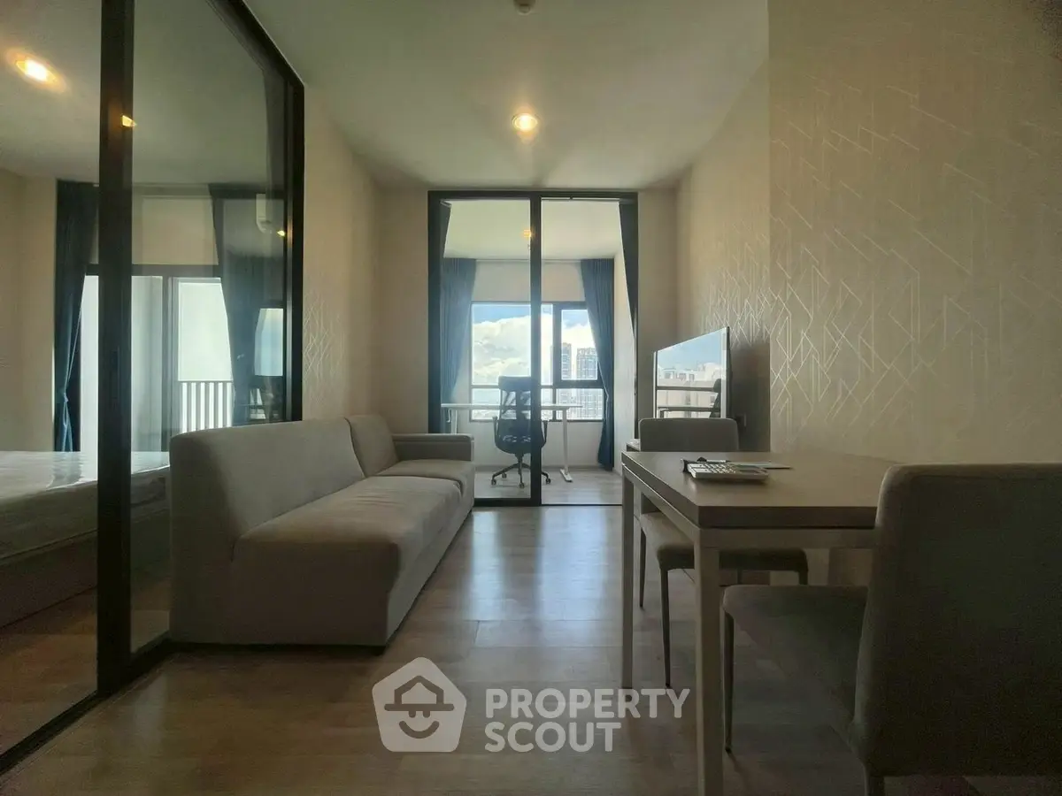 Modern living room with glass partition and city view, featuring sleek furniture and natural light.