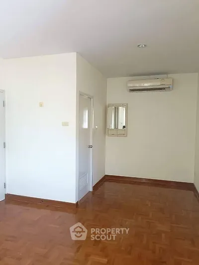 Spacious empty room with wooden flooring and air conditioning, ideal for customization.