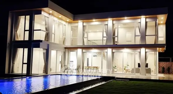 Stunning modern villa with illuminated pool and expansive glass facade at night.
