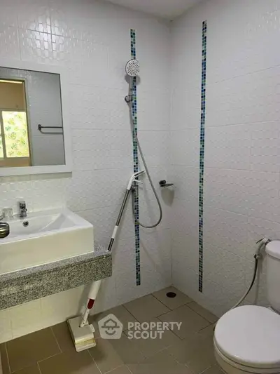Modern bathroom with shower, sink, and toilet in a tiled setting.