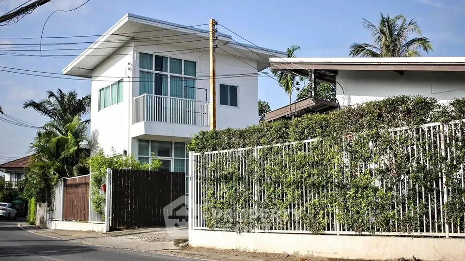 Charming two-story modern home with a lush green hedge fence, featuring a spacious balcony and large windows for ample natural light.