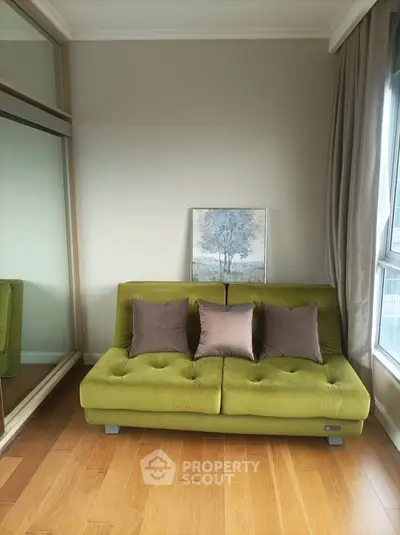 Stylish living room with green sofa and elegant decor, featuring large window and wooden flooring.