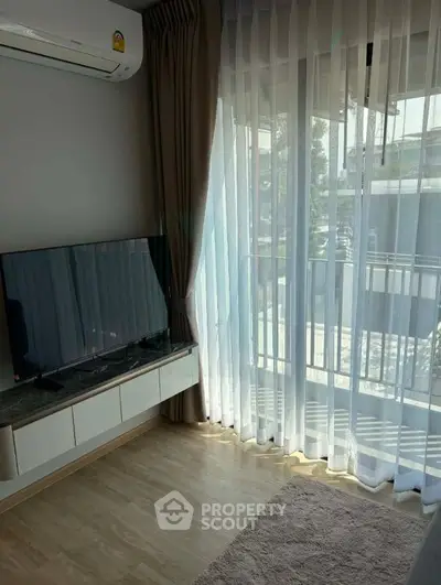 Modern living room with large window and balcony view, featuring sleek TV and air conditioning.
