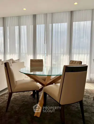 Elegant dining area with glass table and plush chairs in a modern apartment with floor-to-ceiling windows.