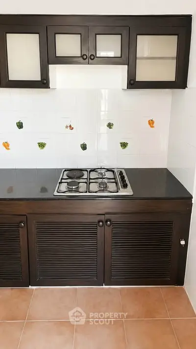 Charming kitchen with dark wood cabinets and gas stove, featuring decorative fruit tiles for a cozy touch.
