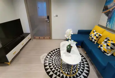 Modern living room with stylish decor and vibrant colors, featuring a blue sofa and geometric patterned rug.