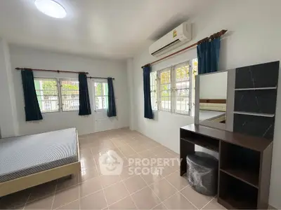 Spacious bedroom with natural light, featuring a bed, desk, and air conditioning.