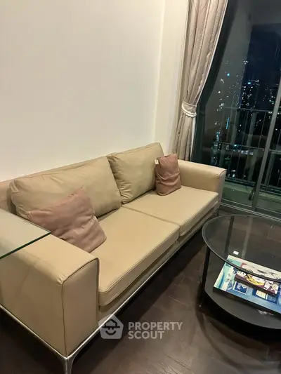 Modern living room with beige sofa and glass coffee table, city view from window.