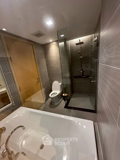 Modern bathroom with glass shower, bathtub, and sleek fixtures in luxury apartment.