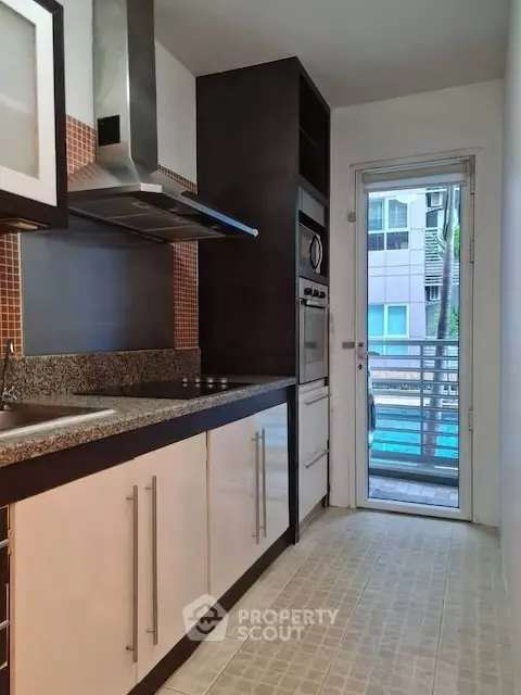 Modern kitchen with sleek cabinetry and stainless steel appliances, featuring a view of the balcony.
