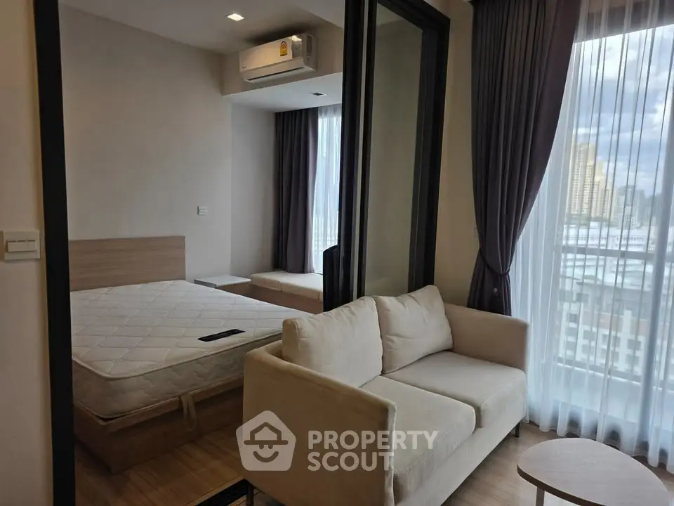 Modern studio apartment with cozy living area and large windows offering city views.