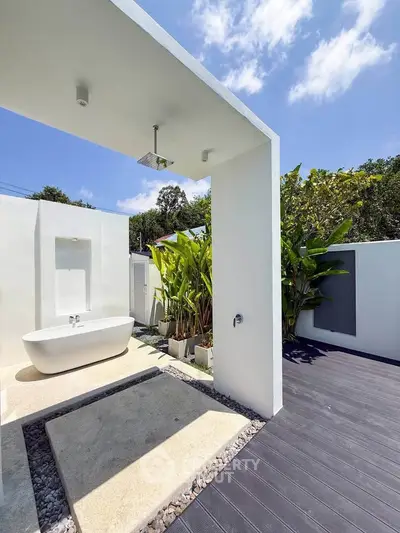 Luxurious outdoor bathroom with modern bathtub and shower, surrounded by lush greenery and blue sky.