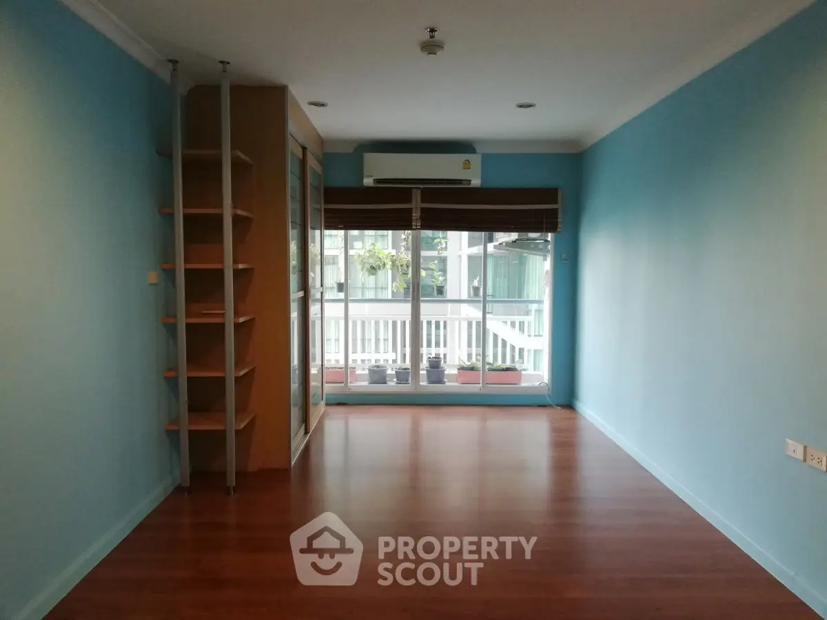 Spacious empty room with wooden flooring and large window, ideal for customization.