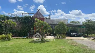 Charming countryside home with lush garden and carport under a clear blue sky.