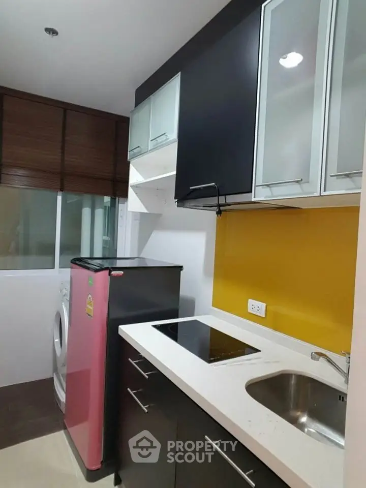 Modern kitchen with sleek black cabinets, vibrant yellow backsplash, and compact appliances.
