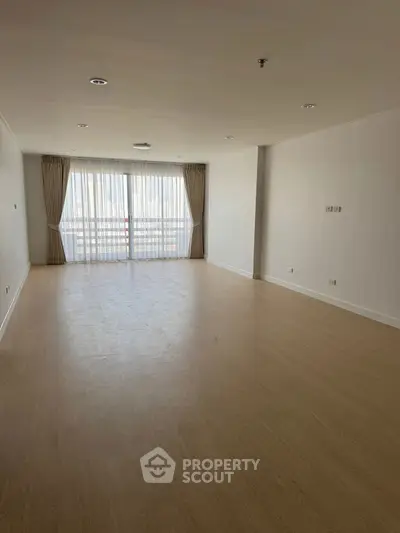 Spacious empty living room with large windows and wooden flooring, perfect for customization.