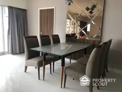 Elegant dining room with glass table and upholstered chairs, featuring mirrored wall accents.