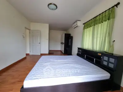 Spacious bedroom with wooden flooring and natural light, featuring a large window and modern furnishings.
