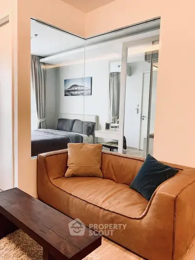 Modern living room with stylish leather sofa and large mirror reflecting bedroom