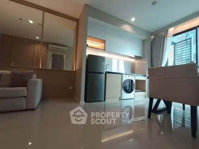 Modern open-plan living room with sleek kitchen and appliances, featuring a washing machine and fridge.