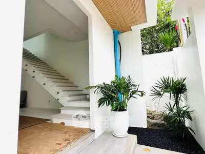Modern entrance with sleek staircase and lush greenery, showcasing contemporary architectural design.