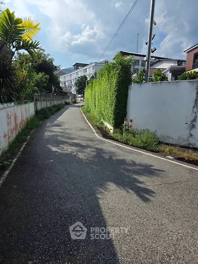 Charming residential street with lush greenery and modern apartment buildings under a clear blue sky.