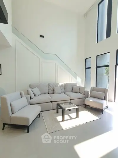 Spacious modern living room with high ceilings and large windows, featuring elegant furniture and natural light.