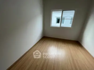 Spacious empty room with wooden flooring and large window in modern apartment.