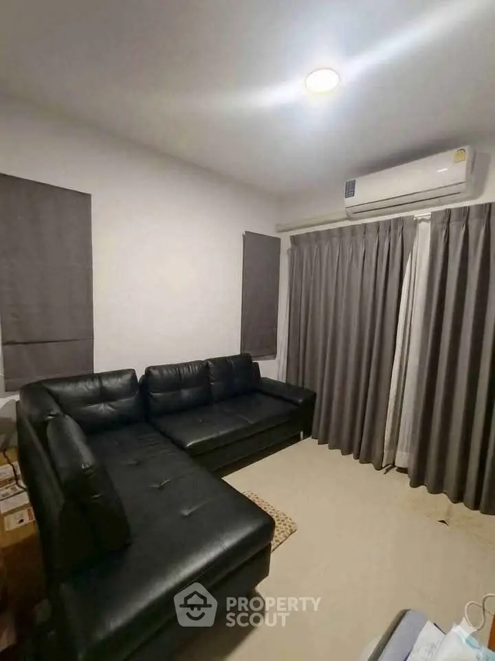 Cozy living room with black leather sectional sofa and air conditioning, perfect for relaxation.