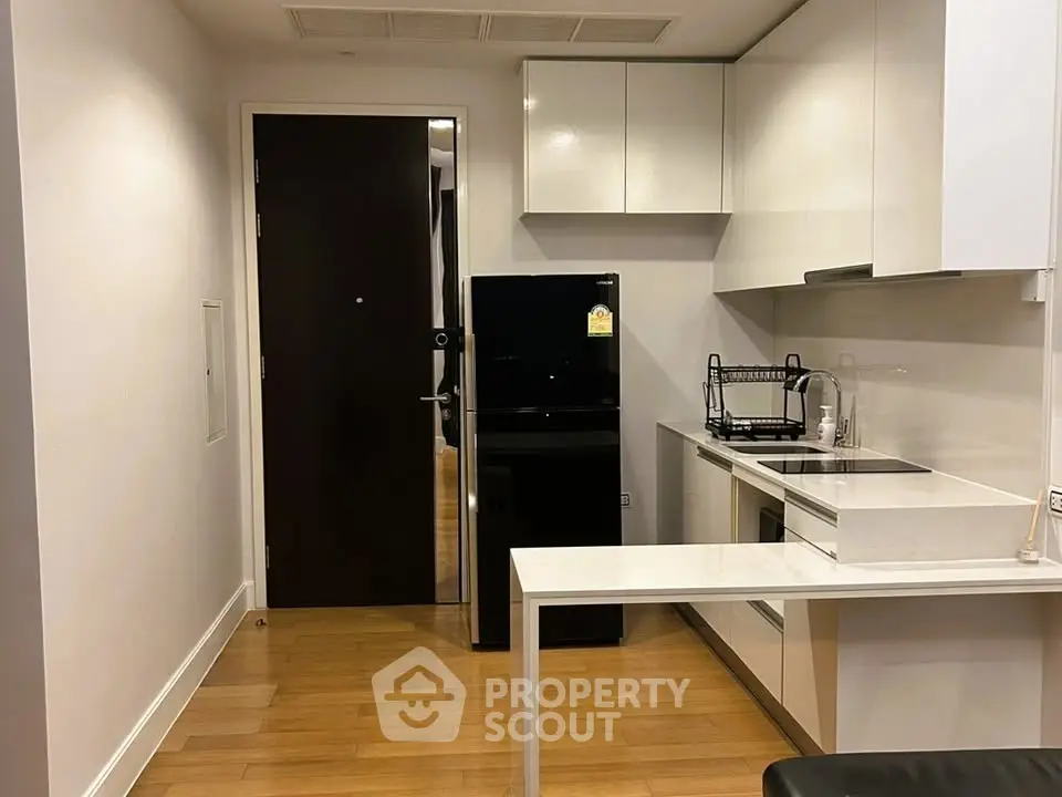Modern kitchen with sleek black fridge and white cabinetry in compact apartment