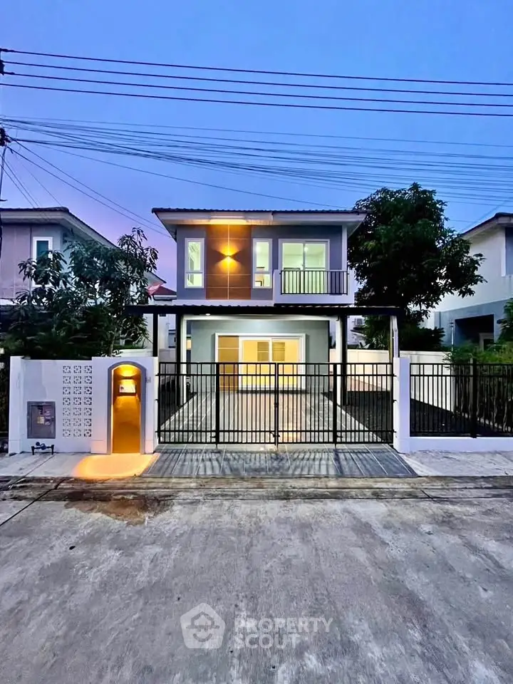 Modern two-story house with gated entrance and driveway, featuring contemporary architecture and evening lighting.
